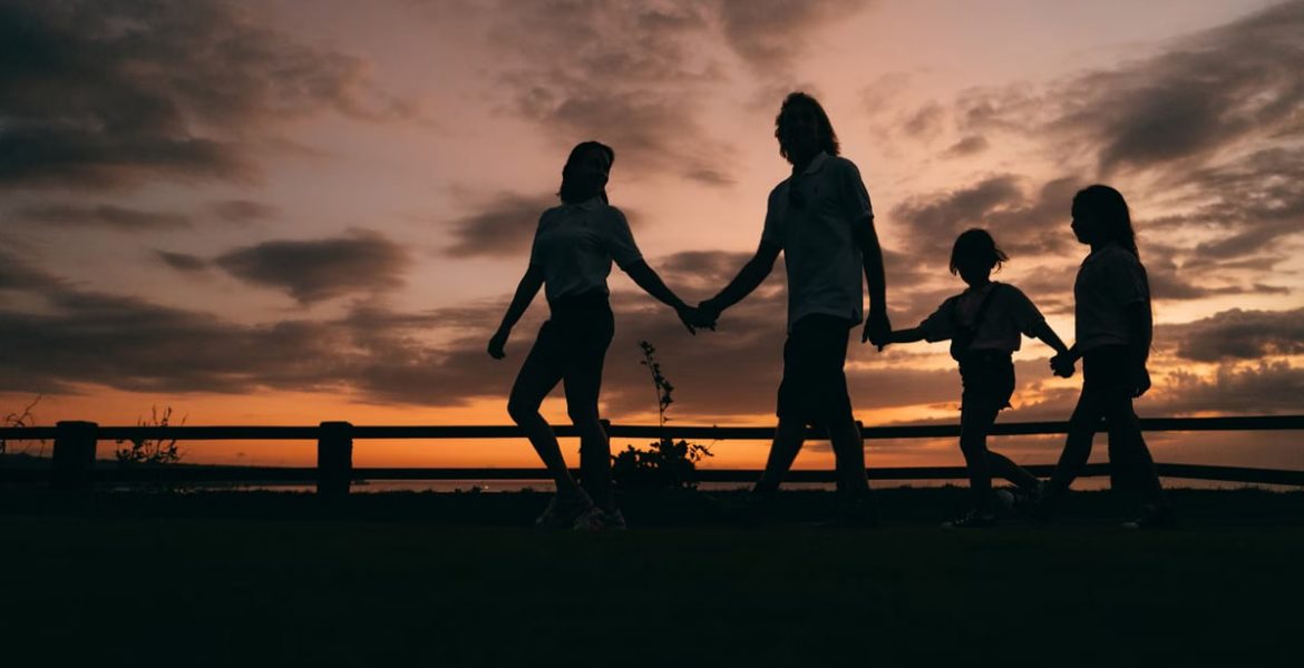 A family walks hand in hand against a vibrant sunset, evoking togetherness and peace.