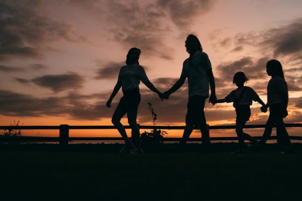 A family walks hand in hand against a vibrant sunset, evoking togetherness and peace.