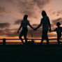 A family walks hand in hand against a vibrant sunset, evoking togetherness and peace.