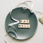 Flat lay of scrabble tiles spelling 'eat well' on a plate with a tape measure, promoting healthy eating.